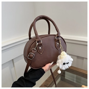 Detail einer dunkelbraunen Mini-Boston-Tasche mit flauschigem Monster-Anhänger und Griff