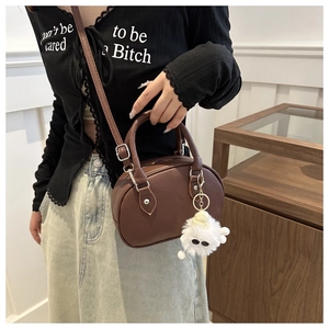 Braune Mini-Bowlingtasche im Detail mit Ledertextur und weißem Plüschtier-Anhänger