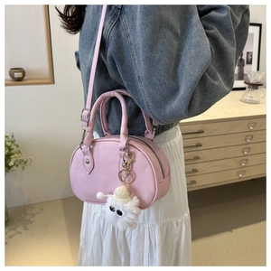 Detail einer hellrosa Mini-Handtasche mit Doppelgriffen und süßem weißem Plüsch-Anhänger