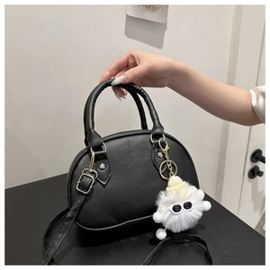 Details der schwarzen halbkreisförmigen Tasche mit Silberzipper und weißem Plüschanhänger