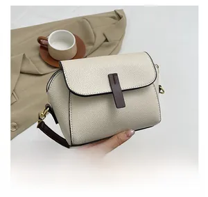 Detailed macro view of cream-white pebbled faux leather bag with dark brown strap and gold hardware