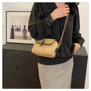 Detail of a beige pebbled leather crossbody bag featuring a brown strap and matte gold buckle