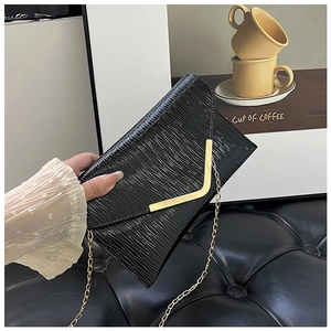 Détail du sac enveloppe noir avec texture épi et bandoulière en chaîne dorée chic