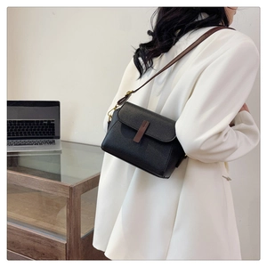 Detail of black pebbled leather crossbody bag with brown trim and gold hardware accents