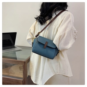 Detail view of smog blue leather crossbody bag with brown strap on a model outfit