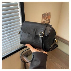 Detail of black pebbled leather crossbody bag with golden hardware and flap closure