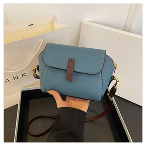 Detailed view of smog blue cross-body bag with litchi grain texture and gold metal accents