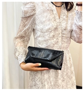 Detail of elegant black crocodile pattern envelope clutch with golden chain strap