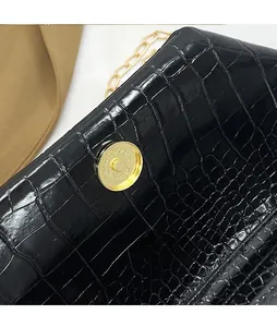 Detail view of black crocodile pattern leather bag with golden magnetic clasp and chain strap