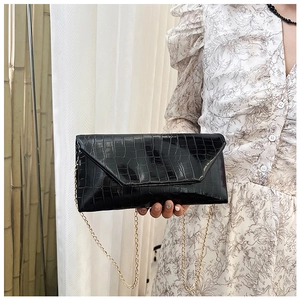 Detail of black crocodile texture clutch with gold chain strap held by a model