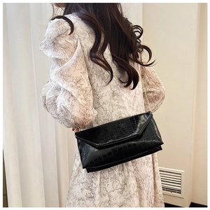 Detail of black crocodile-embossed envelope clutch with gold chain strap on shoulder