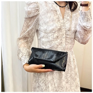 Detail of black crocodile pattern envelope clutch bag with thin gold chain strap