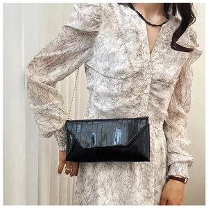 Close-up of black crocodile pattern envelope crossbody bag with gold chain strap
