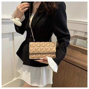 Détail d'un sac bandoulière matelassé beige avec chaîne dorée et boucle sur mannequin