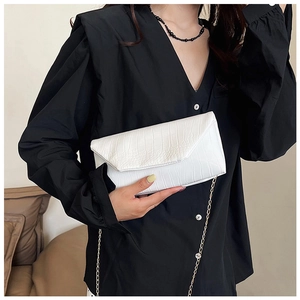 Detail of white crocodile embossed envelope bag with gold chain strap on black shirt