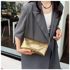 Detail of a golden chain crossbody bag featuring a premium faux crocodile skin texture