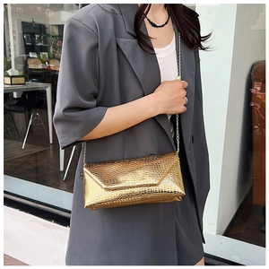 Close-up of golden envelope clutch bag with crocodile texture and metal chain strap