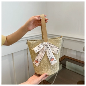Detailed close-up of woven straw bucket bag with leather handle and decorative silk scarf