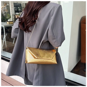 Detailed view of glossy gold metallic chain bag with crocodile texture on a model's back