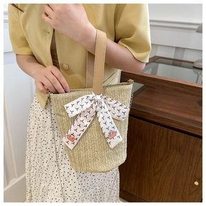 Detail of woven straw tote bag with brown leather handle and geometric silk scarf decoration