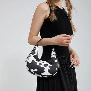 Sac croissant à imprimé vache avec bandoulière noire et détails dorés porté par un modèle