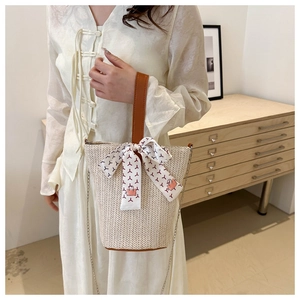 Detail of woven straw bucket bag featuring leather handles and printed silk scarf