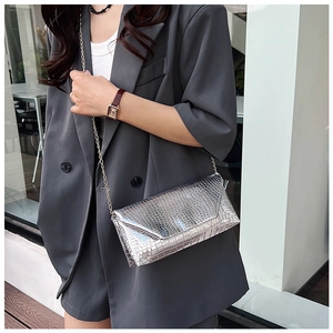 Detail of silver crocodile embossed envelope bag with gold chain strap on a grey suit