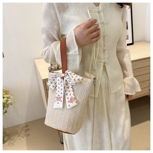 Detail view of woven bucket bag featuring brown leather handle and floral silk scarf charm