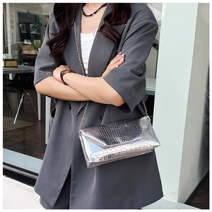 Detail of silver crocodile-embossed envelope bag with golden metallic chain strap
