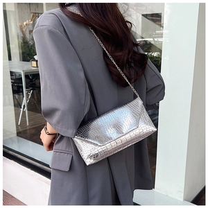 Detail of silver metallic envelope chain bag with crocodile pattern texture on female model