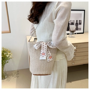 Detail of woven straw bucket bag featuring white silk scarf and silver chain strap