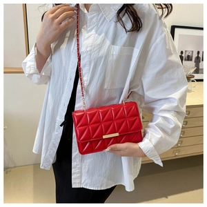 Détail d'un sac à bandoulière matelassé rouge avec barre dorée et bandoulière chaîne
