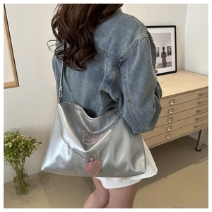 Sac bandoulière argenté avec broderie papillon rose et breloque cœur porté par mannequin