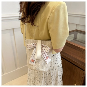 Detail of cream woven bucket bag with silk scarf ribbon and slim metal chain strap