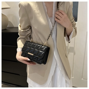 Détail du sac matelassé noir à chaîne sur blazer beige montrant la boucle métallique