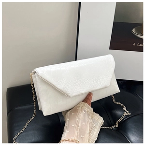Close-up of white crocodile pattern crossbody bag with golden chain strap on a sofa
