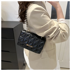 Sac à bandoulière matelassé noir avec chaîne dorée porté par un mannequin en veste