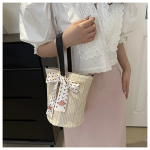 Detail of cream woven straw bucket bag with black leather handle and pattern scarf