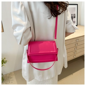 Detail of a bright magenta minimalist crossbody bag showing stitching and glossy finish
