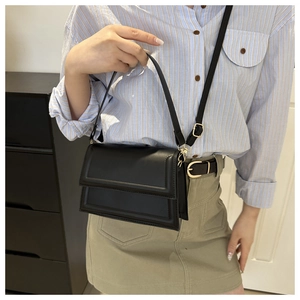 Detail of a black square crossbody bag with gold hardware worn with a casual outfit