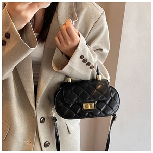 Close-up of black quilted oval baguette bag with gold metal clasp on beige blazer