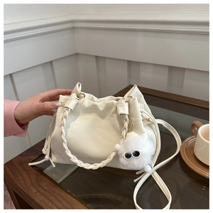 Close-up of white bucket bag with woven handle and plush monster charm on wooden table