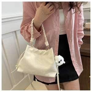 Detail of cream white bucket bag with braided handle and plush monster pendant charm