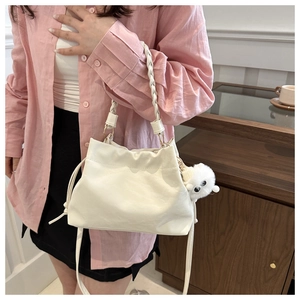Close-up of white drawstring bucket bag with plush charm and woven handle in lifestyle setting