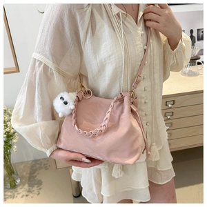 Detail of light pink bucket bag with braided handle and white plush charm on a model