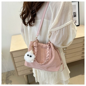 Detail of light pink nylon bucket bag featuring woven handle and plush monster charm