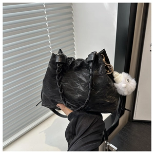 Detail of black drawstring cloud bucket bag with woven handle and plush charm