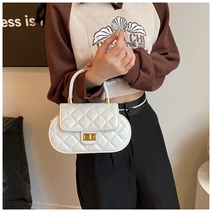 Detail of a white quilted oval baguette bag with a gold twist lock and rounded top handle