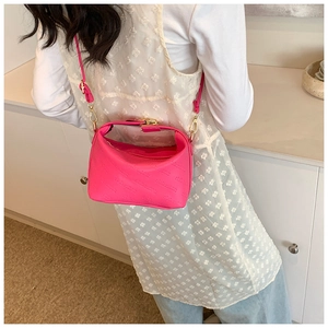 Detail of hot pink crossbody bag with embossed lettering and golden hardware on model