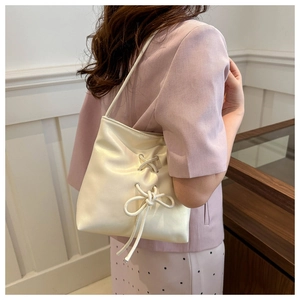 Detail of cream white leather bucket bag featuring a decorative bow knot and shoulder strap